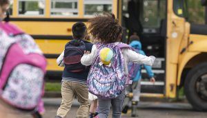 Four schoolchildren run to get on a school bus parked outdoors.