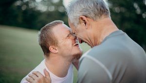 An older man and a disabled teenager laughing together in a field