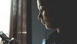 A woman looks down at the screen of her cell phone and frowns