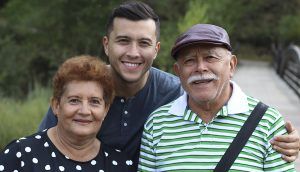 An older man, older woman, and younger man look forward and smile outside