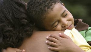 A young boy leans on a woman's shoulder while hugging her