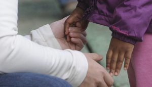 A seated adult's hands holding the hands of a small child standing in front.