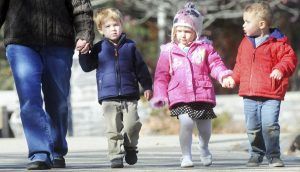 An adult and three small children hold hands as they walk together