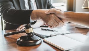 An attorney shakes hands with a client seated on the opposite side of a desk